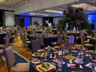 Formal ballroom banquet with navy linens, plated dinners, and tall floral centerpieces by Michaelis Events – Top Event Planners in Louisville KY & Best Wedding Caterers.