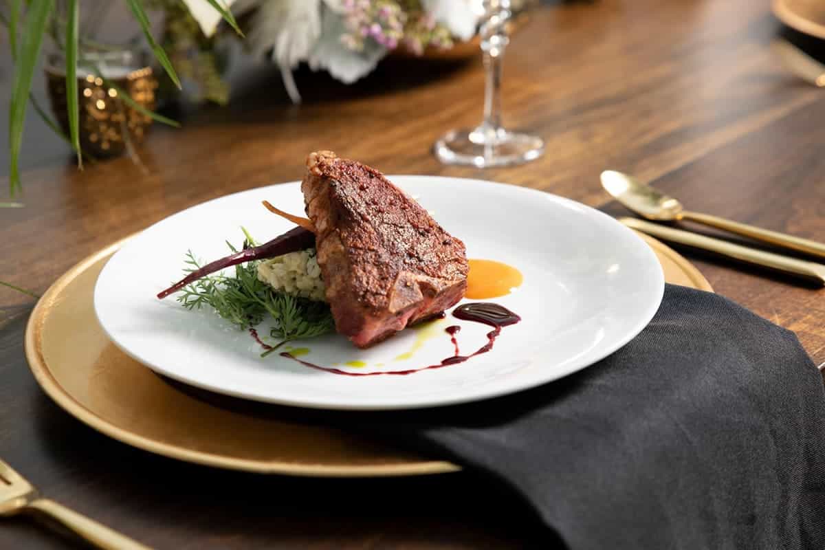Plated gourmet entrée of seared lamb over risotto with carrot garnish and sauce, styled by Michaelis Events – Top Event Planners in Louisville KY & Best Wedding Caterers.