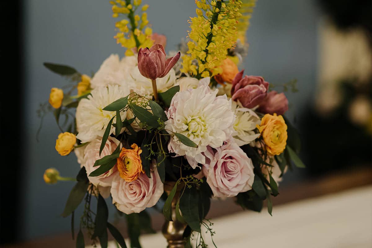 Elegant wedding centerpiece featuring blush roses, white dahlias, tulips, and yellow ranunculus designed by Michaelis Events – Top Event Planners in Louisville KY & Best Wedding Caterers.