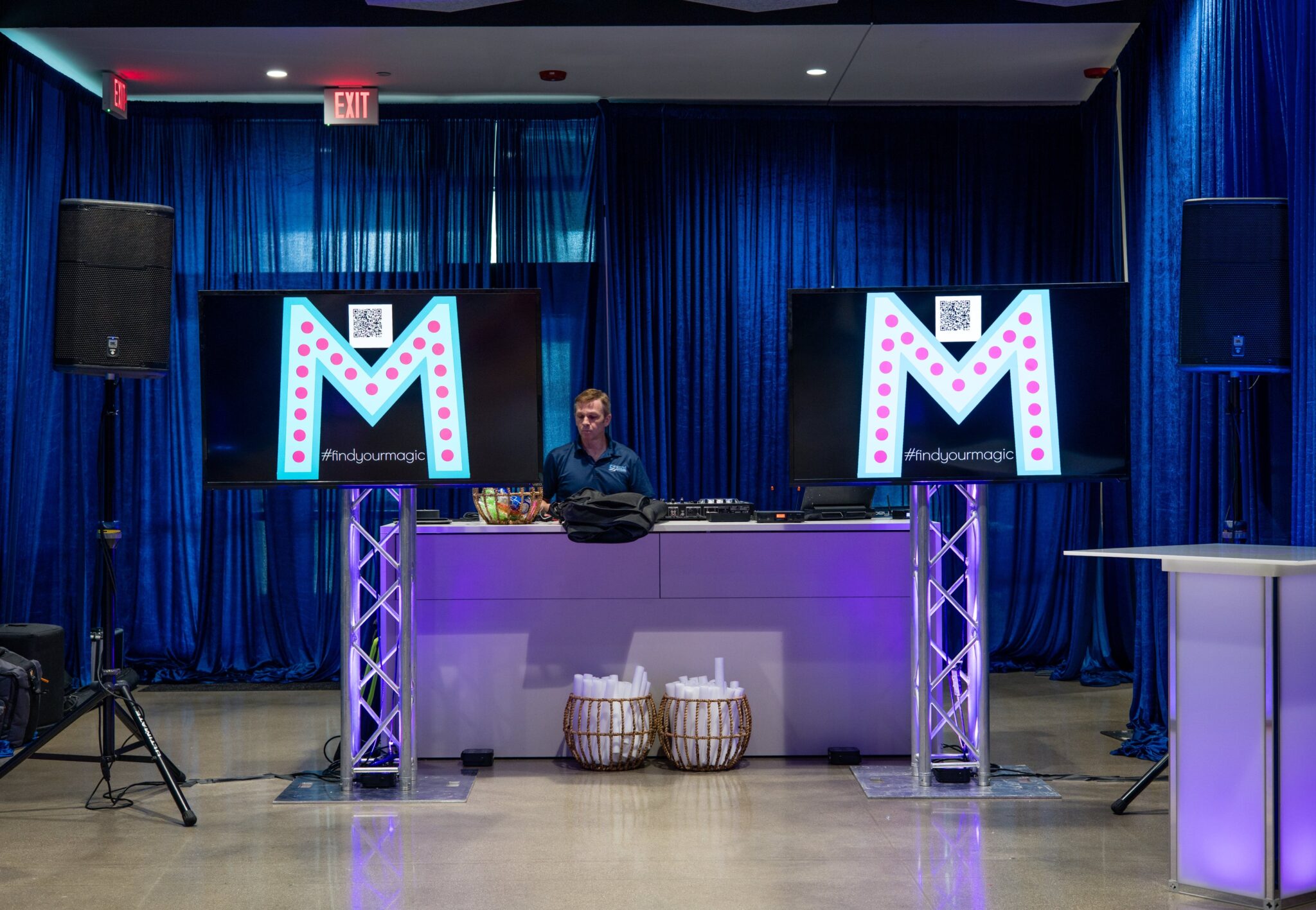 DJ booth with dual screens displaying a stylized “M” logo and #findyourmagic, set against deep blue drapery at a Louisville Bat Mitzvah designed by Michaelis Events. Captured by TIMB Photography.